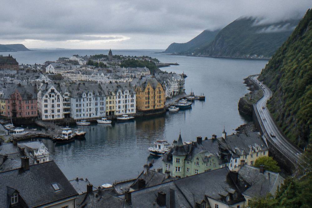 A winding coastal road along a fjord with steep green mountainsides dropping into dark water