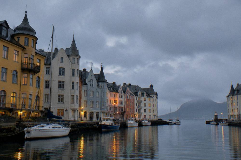 A small Norwegian coastal town at dusk with warm lights reflecting on calm harbor water