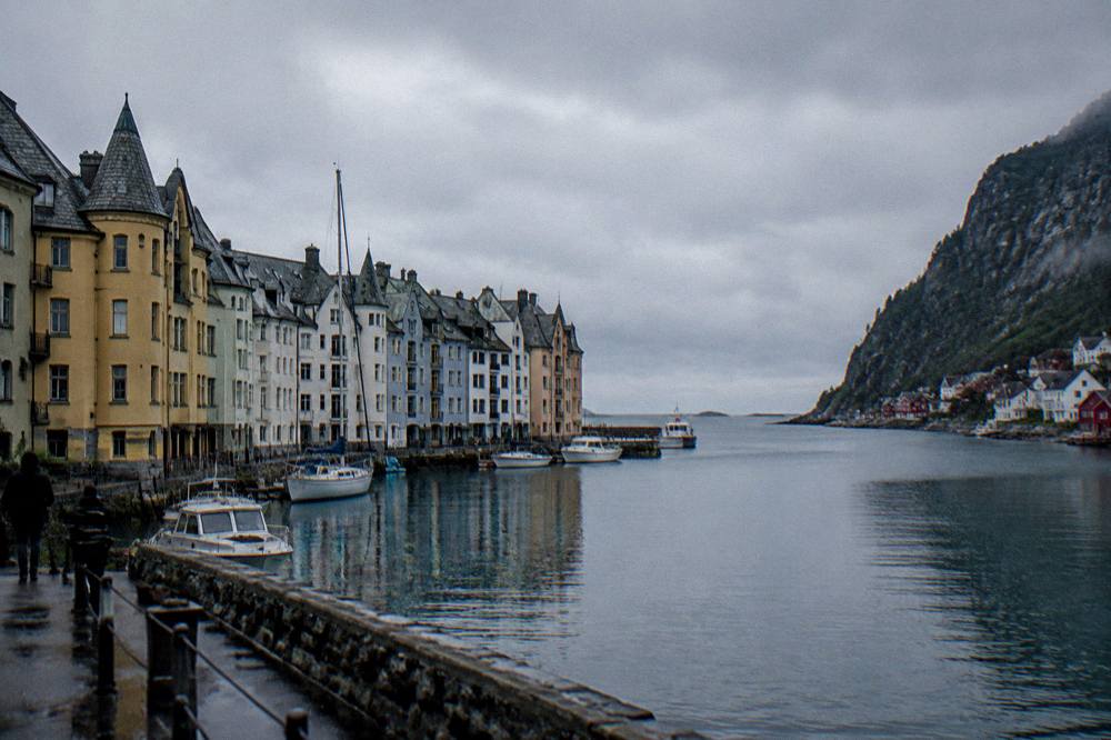 A Norwegian fjord village with steep cliffs rising behind small red and white houses at the waterline