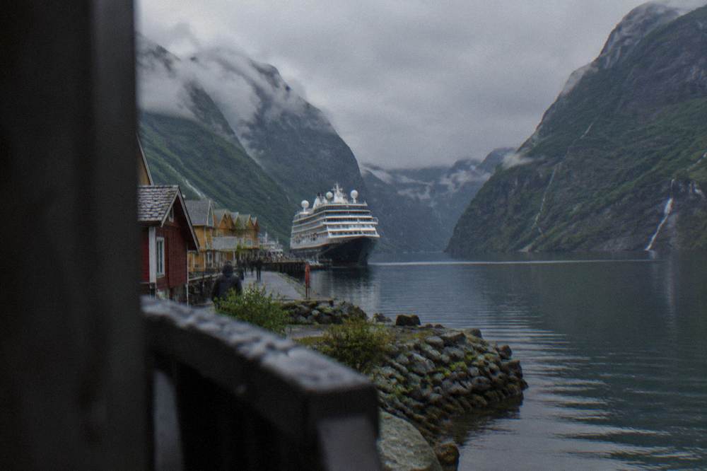 A cruise boat moored at Flåm village with steep green mountainsides rising above the fjord water