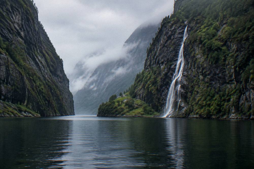 The narrow Nærøyfjord seen from the water, with near vertical rock walls and a cascade falling toward the fjord