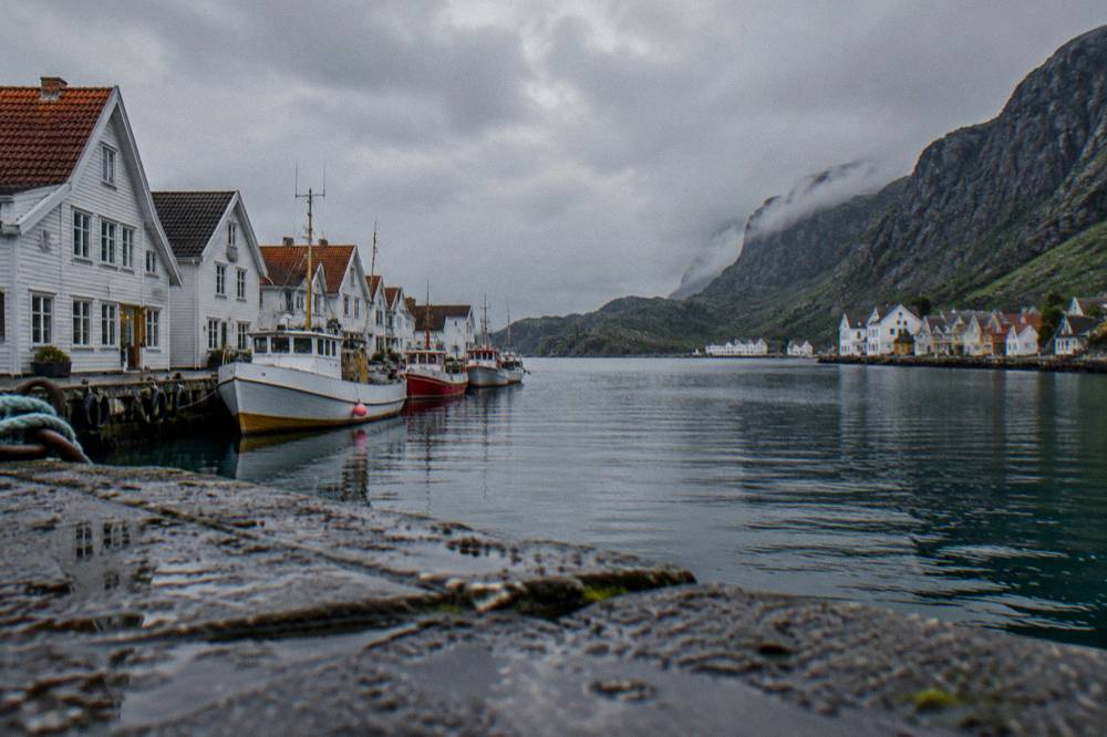 A narrow arm of a Norwegian fjord with a small village of houses at the water's edge beneath steep cliffs