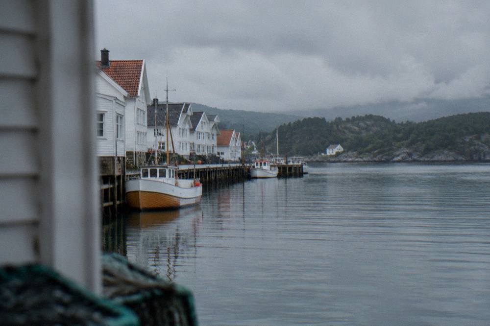 A small boat moored at a wooden pier on a Norwegian fjord with forested hills in the background