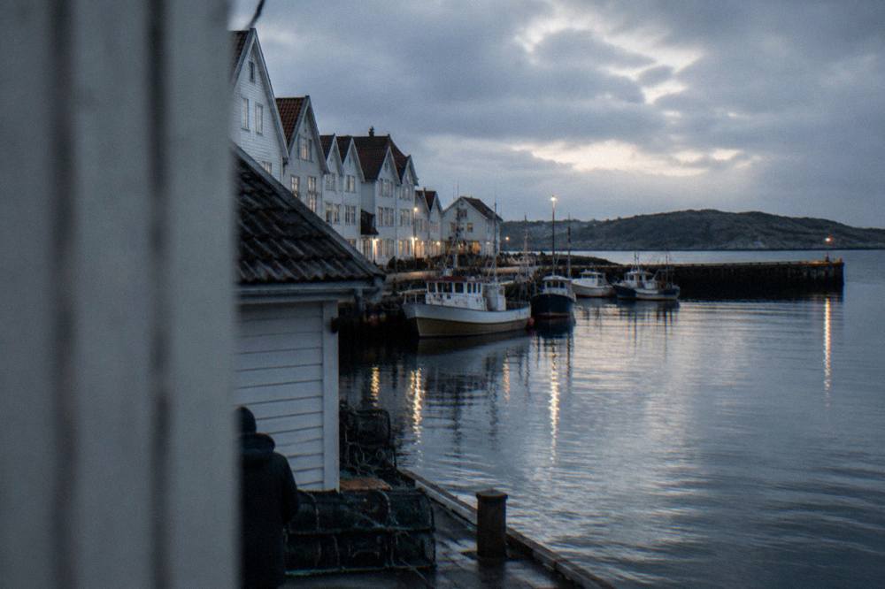 The harbour of a Norwegian coastal town at dusk with boats, wooden piers and lights reflecting on calm water