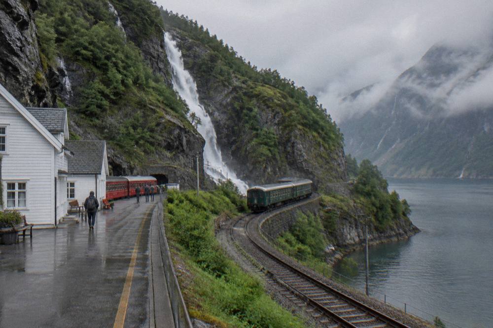 A white mountain railway station with a red train waiting at the platform