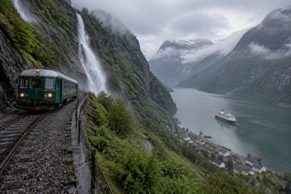 A fjord cruise boat on calm water between steep cliffs with a small village on the shore