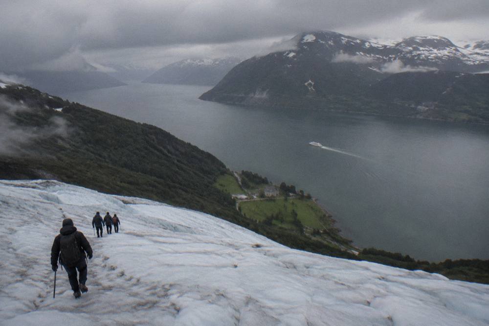 A white tour boat sailing across a wide fjord with snow-patched mountains on both sides