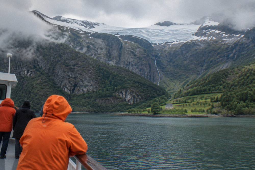 Passengers in orange waterproof jackets standing on the deck of a tour boat as it passes a cliff face above dark water