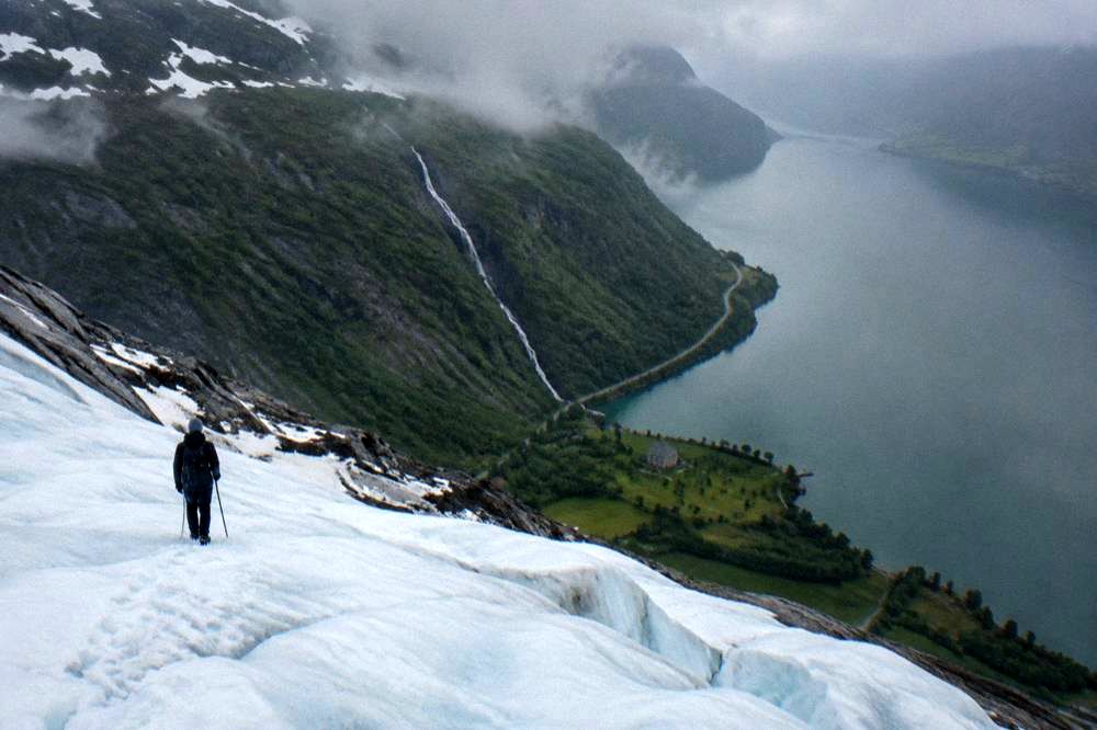 A tall thin waterfall falling down a green rock wall beside a narrow fjord road