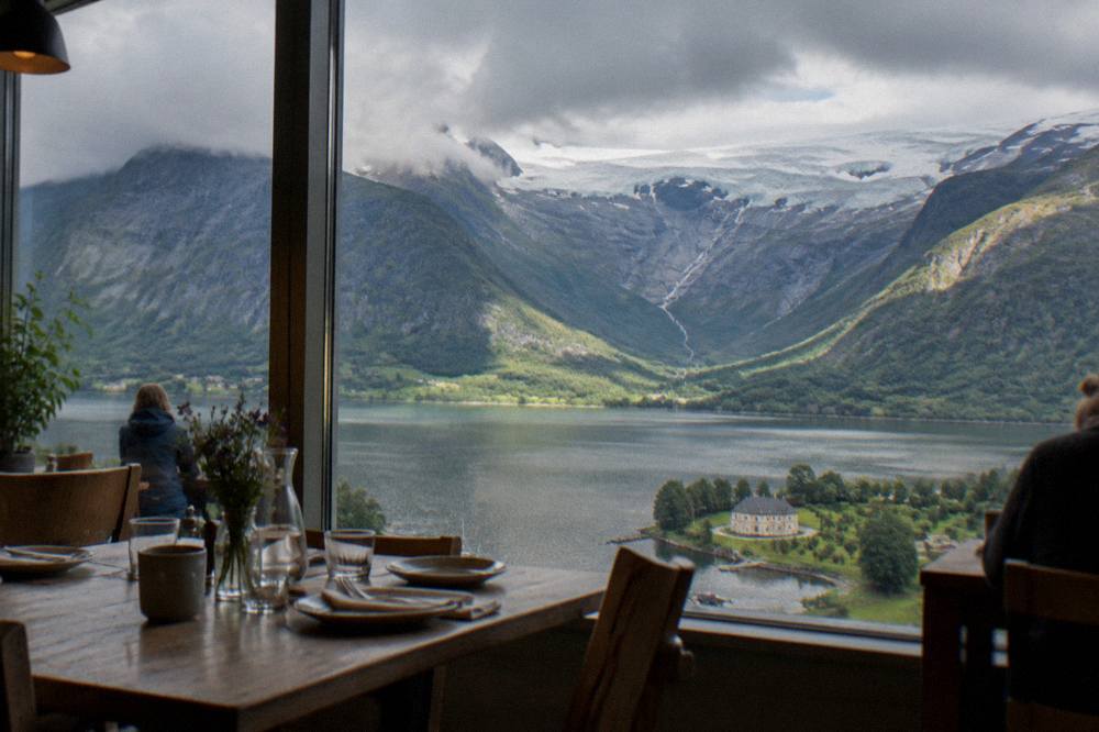 Wooden tables set for lunch inside a small Norwegian café with a view of a fjord through the window