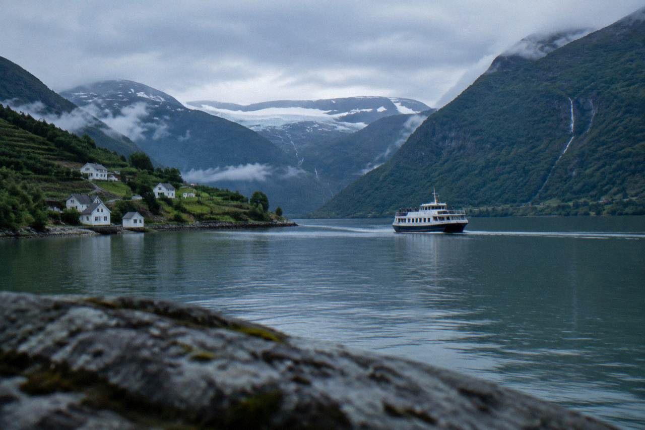 A tour boat crossing calm Hardangerfjord water below steep green mountainsides
