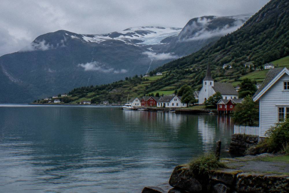 A village church and wooden houses beside the water on a calm fjord morning