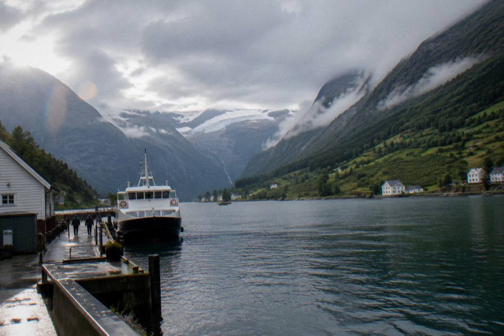 A small ferry docked at a Hardangerfjord village pier under low clouds
