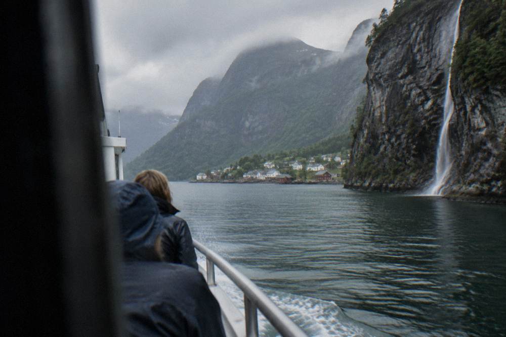 A wide fjord with a small village of wooden houses on the shore and mountains behind