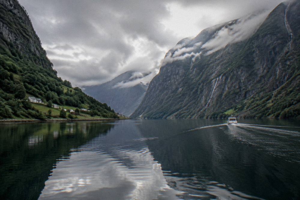 Calm fjord water reflecting steep mountain slopes with a small boat wake
