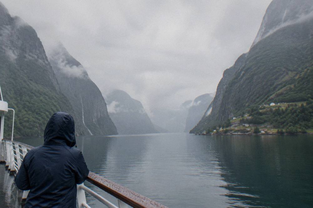 A passenger wearing a rain jacket on the deck of a boat in a fjord