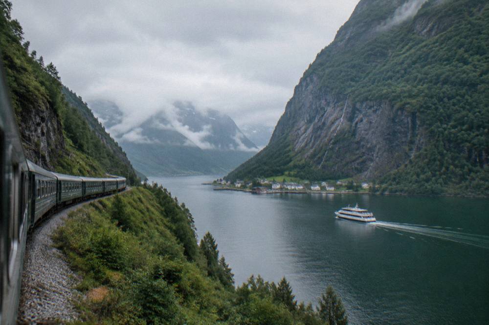 A white sightseeing boat cruising a narrow fjord with sheer cliff walls and a small village at the waterline