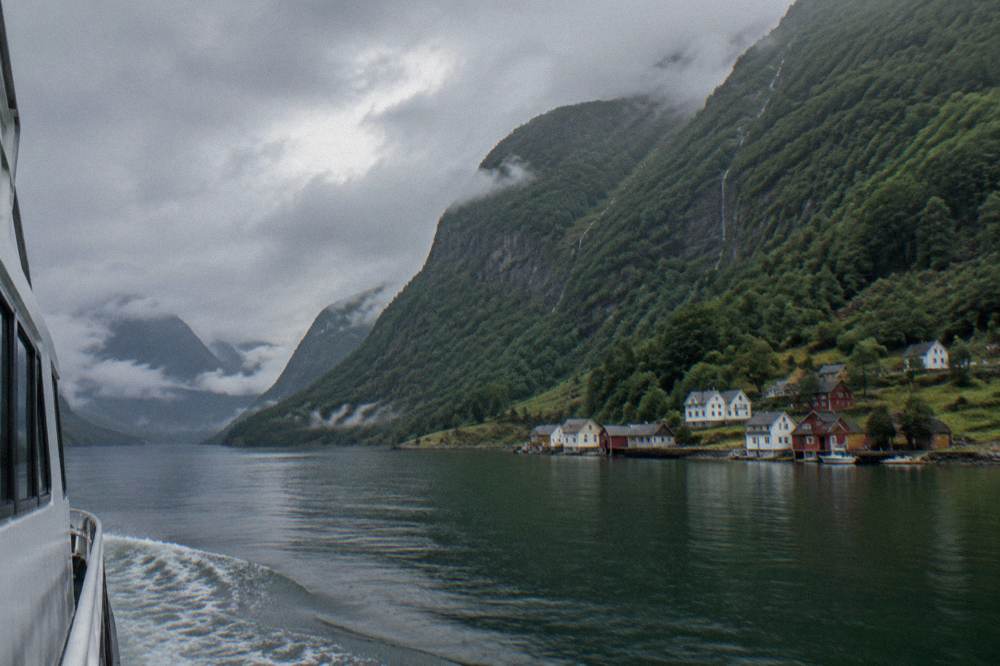 A small fjord village with wooden houses at the water's edge beneath steep mountains in evening light