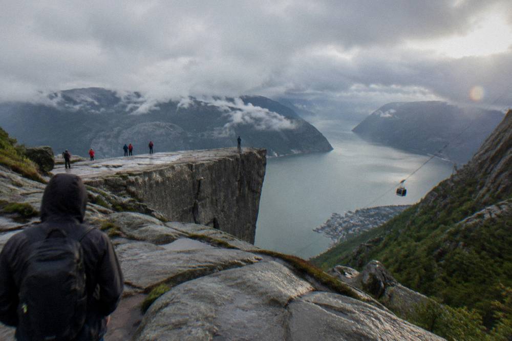 A cable car ascending steep rocky slopes above a city and a fjord arm