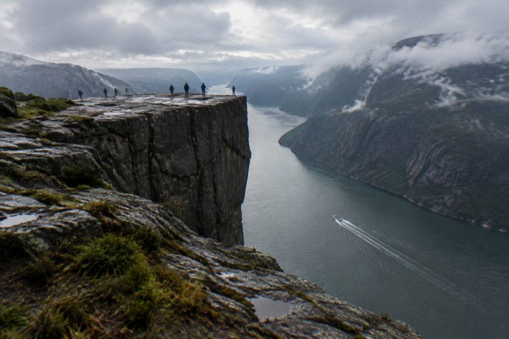 A small open boat speeding along a narrow fjord channel with steep dark rock walls on both sides