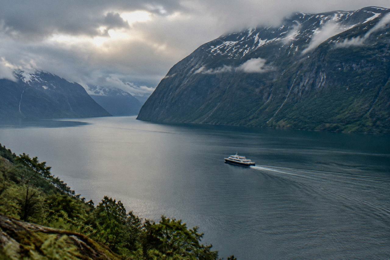 A tour boat crossing calm water on a wide Norwegian fjord with steep green mountains rising on both sides