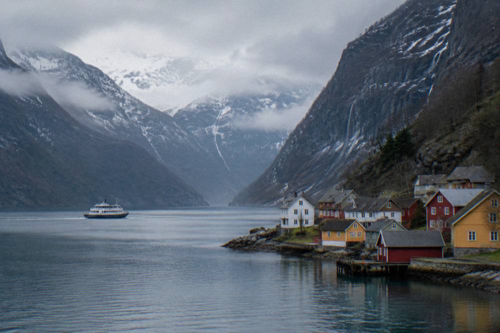 A small village of colourful wooden houses at the water's edge beneath a steep fjord wall