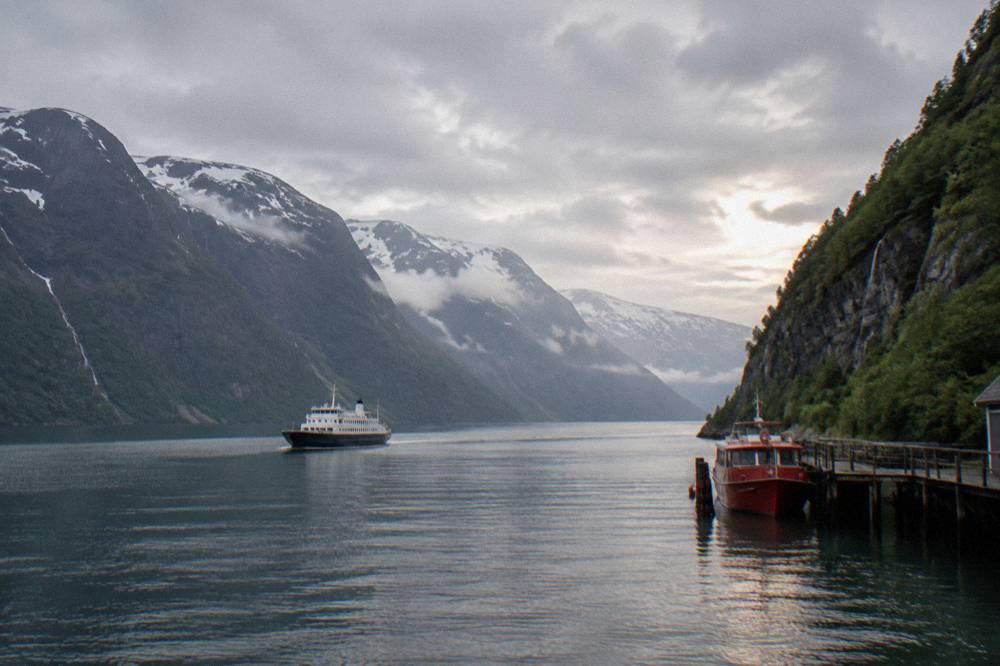A red passenger boat moored at a wooden pier beneath steep forested cliffs
