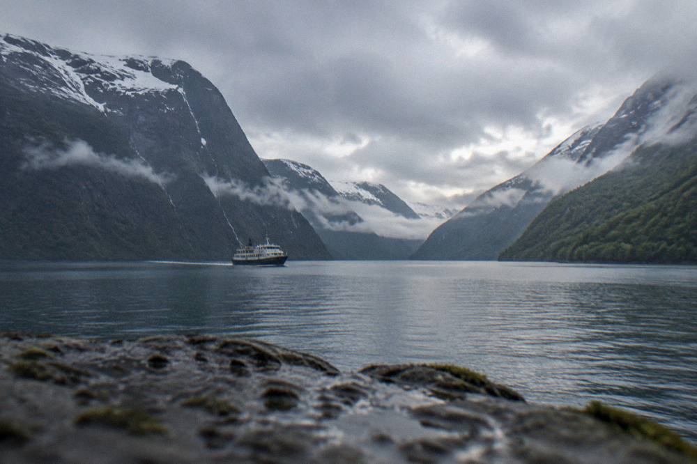 Low cloud drifting between forested mountains above a narrow fjord arm at dusk
