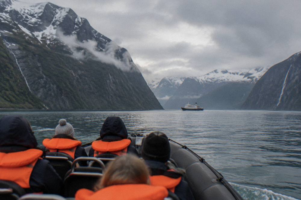 A group of passengers in orange life vests seated in an open RIB boat on a fjord