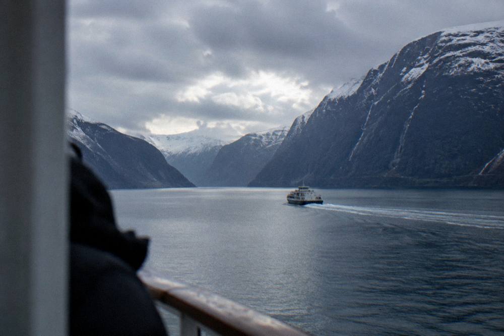A passenger ferry leaving a wake across a broad fjord under a partly cloudy sky
