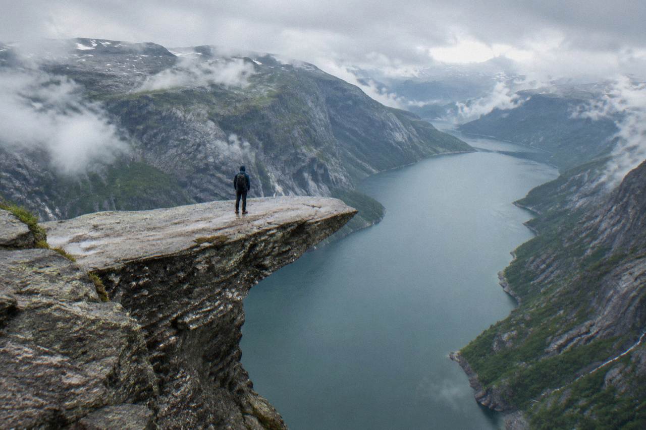 A hiker standing on the flat rock ledge of Trolltunga with the blue fjord water far below