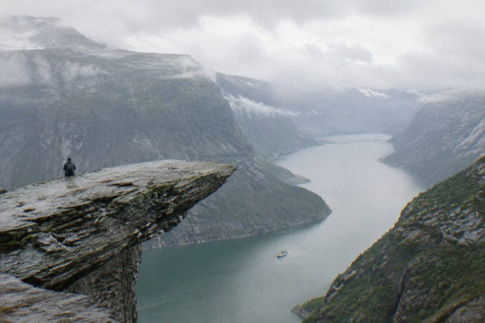 A tour boat on calm green fjord water between steep forested mountain walls