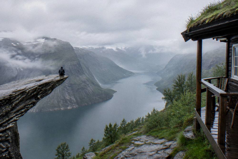 A wooden cabin porch in a green Hardanger valley with a fjord and steep hills behind