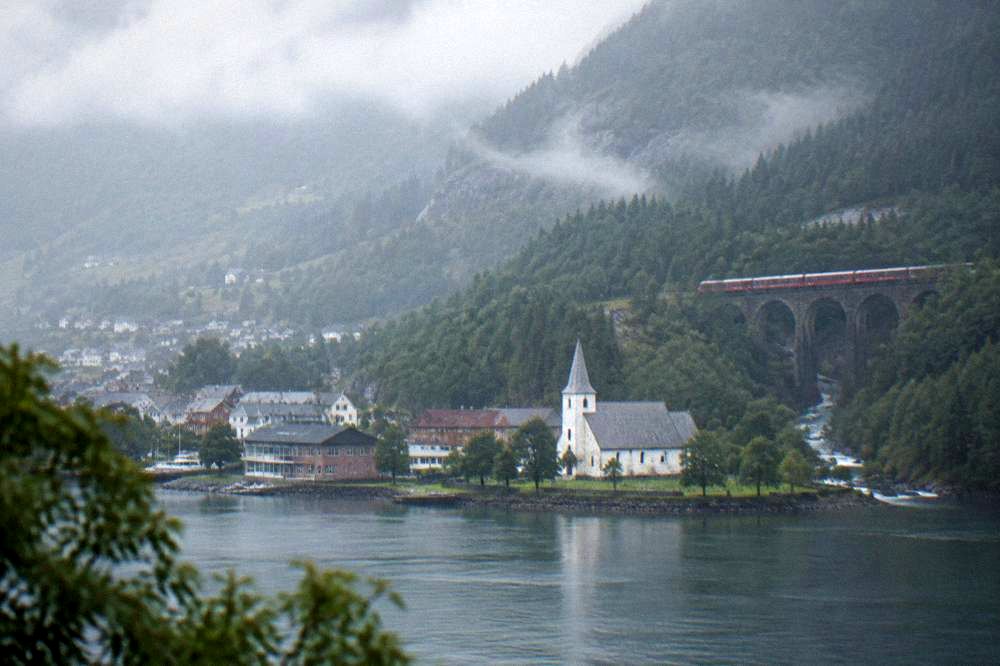 A red mountain train crossing a stone viaduct above a river valley with pine forest