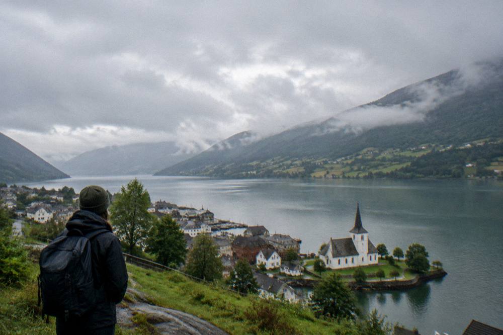 A traveler with a backpack overlooking a wide lake valley with patchwork fields on the far shore