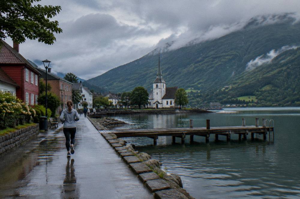 A summer lake town under a partly cloudy sky with a wooden pier reaching into still water