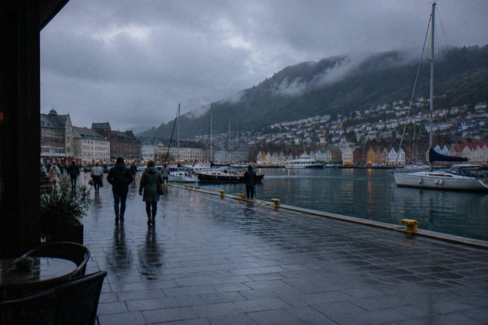 A flat harbour promenade in central Bergen with moored boats and people strolling