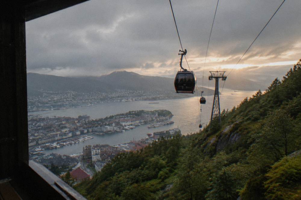 Cable car cabins travelling up a steep green mountain above Bergen with the city below