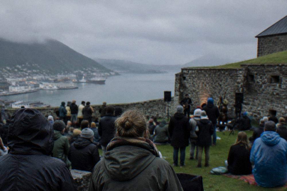A festival crowd gathered on a fortress lawn beside old stone walls in evening light