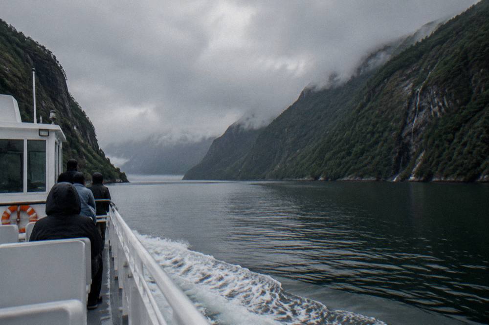 A passenger boat sailing along a narrow fjord channel between steep forested cliffs