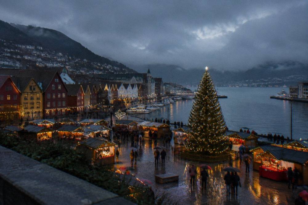 Festively lit wooden market stalls with a large Christmas tree in a Bergen city square