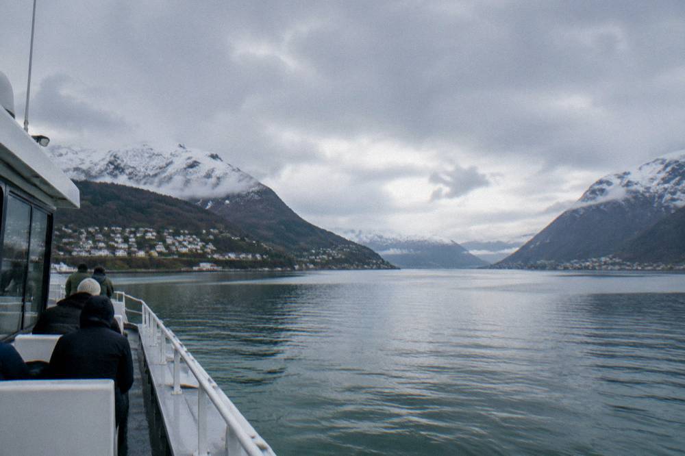 A passenger boat on a calm fjord with snow-dusted mountains on either side near Bergen