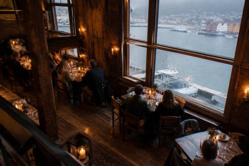 A warmly lit restaurant interior with candles and diners in a historic timber building in Bergen
