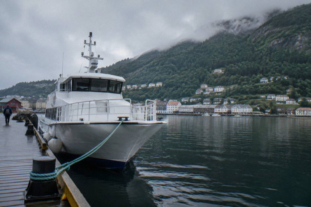 A passenger boat moored at a wooden pier below steep forested hillsides near Bergen