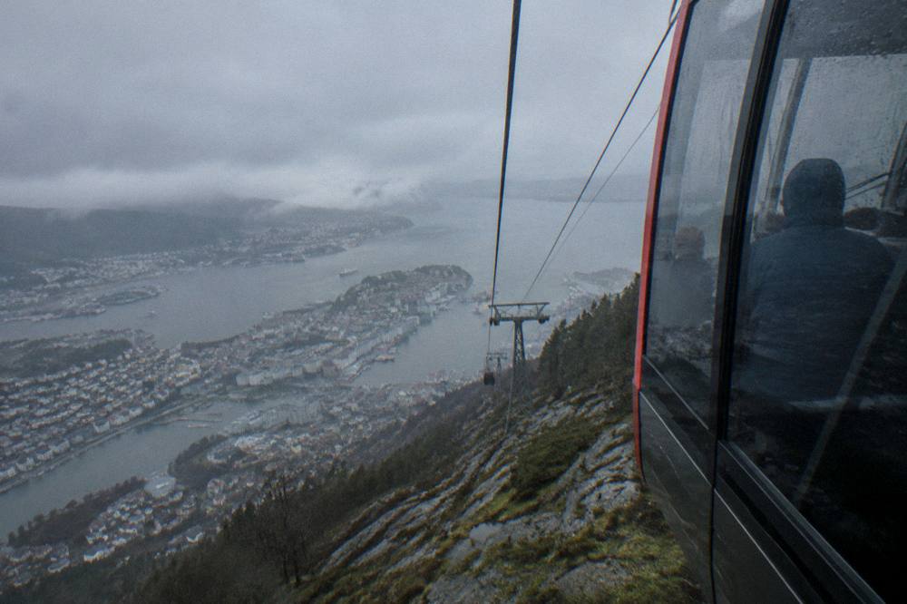 A cable car cabin ascending a steep rocky mountainside above Bergen