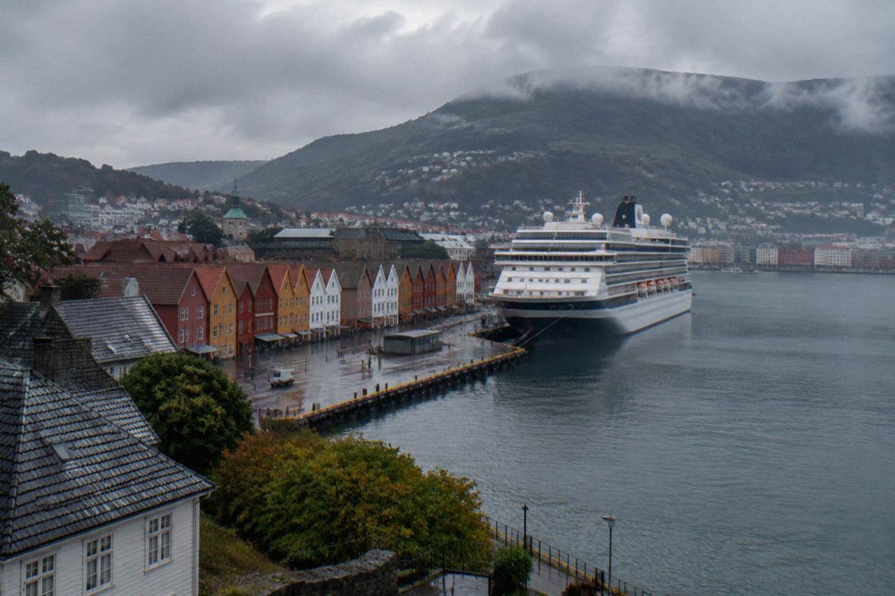 A large cruise ship moored at a quay in Bergen harbour with colourful wooden buildings along the waterfront