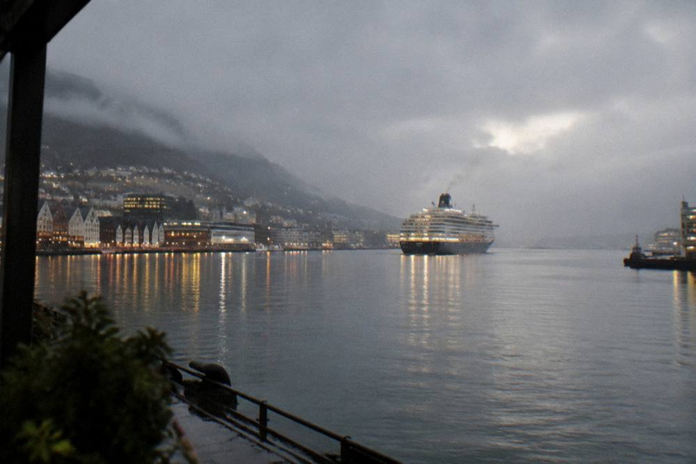 A cruise ship leaving Bergen harbour at dusk with city lights reflecting on the water