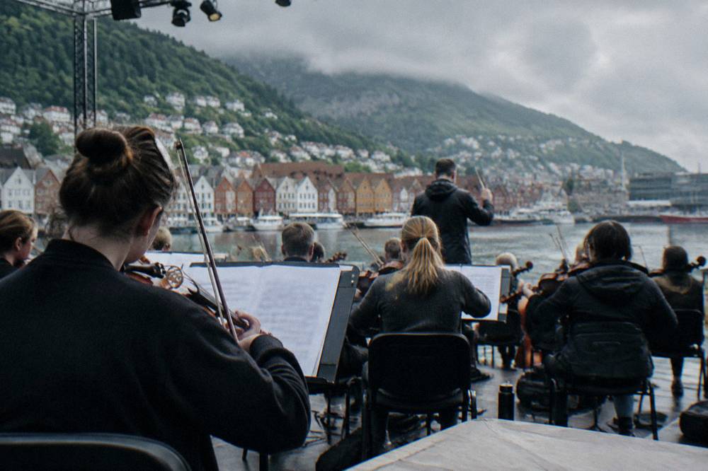 An orchestra rehearsing on an outdoor stage in a Bergen, Norway courtyard before an evening concert