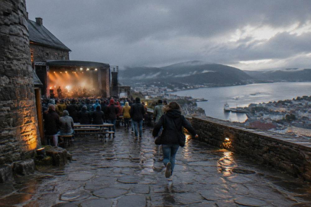 A festival audience gathered in the stone courtyard of a fortress in Bergen, Norway, at dusk