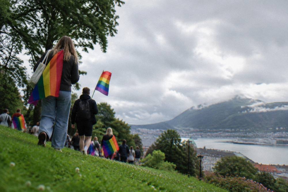 People with rainbow flags walking through a green park in Bergen, Norway, on a summer afternoon